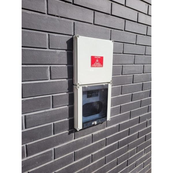 grey semi-recessed generator connection switchboard on a black brick wall outside. 