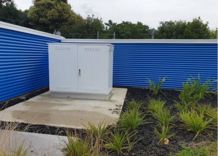 Large white kiosk with fuel pump controls inside bright blue metal fence